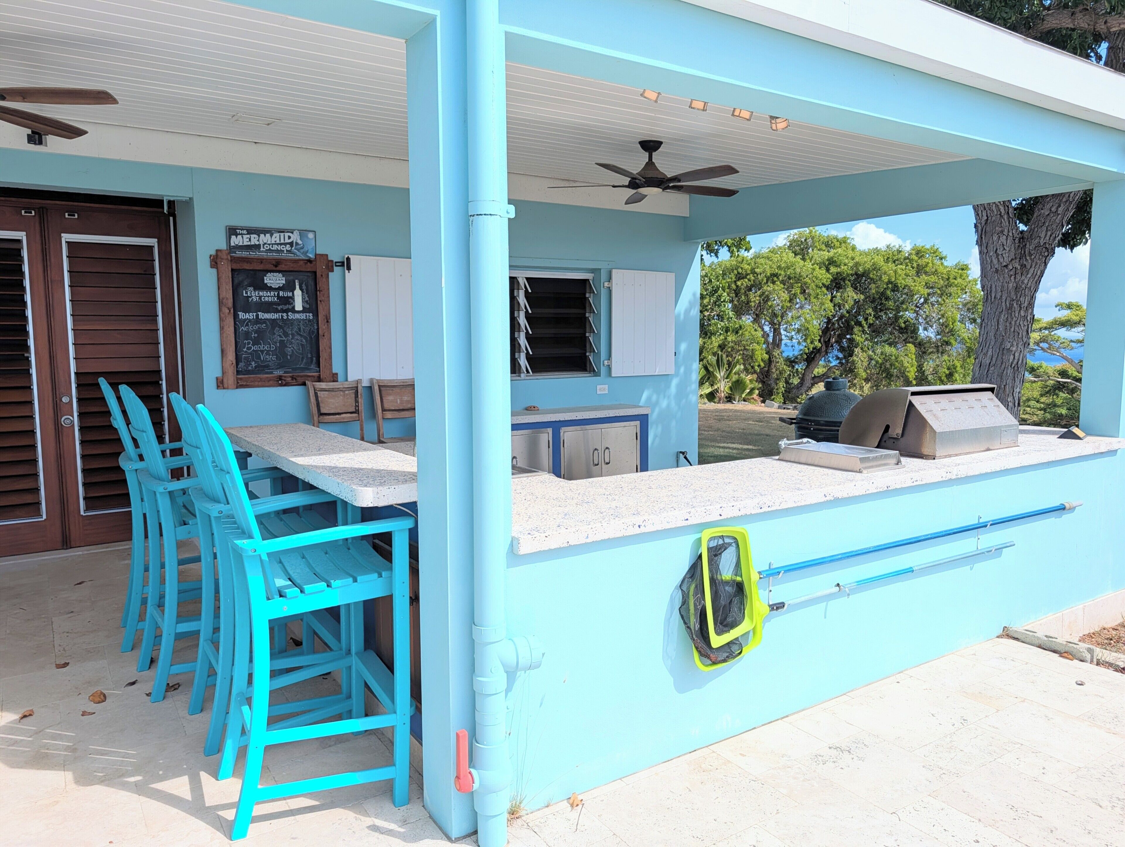 Un espace extérieur abrité avec des chaises bleues, un comptoir et un barbecue.