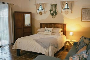 Ein Schlafzimmer mit einem Bett, einem Nachttisch, einer Lampe, einem Fenster mit Vorhängen und einer Wanddekoration.