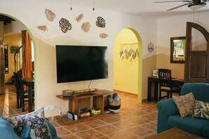 A living room with a flat-screen TV, a wooden entertainment unit, a sofa, and a dining area with chairs and a table. - Fabulous 4-bedroom house with AC & pool 1 km to Playa Grande sleeps 10 (Playa Grande)