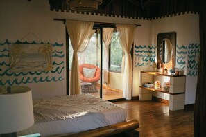 Ein Schlafzimmer mit einem Bett, einem Sessel, einem Schminktisch mit Spiegel und Blick ins Freie.