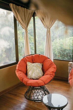 A room with a wooden floor, a round table, and a cushioned chair with a pillow. - Fabulous 4-bedroom house with AC & pool 1 km to Playa Grande sleeps 10 (Playa Grande)