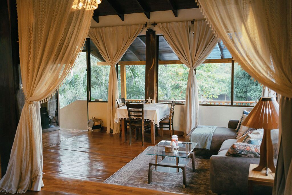 A room with a wooden floor, a glass coffee table, a sofa, and a dining table with chairs.