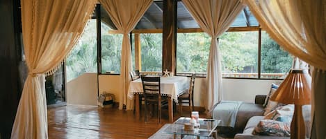 A room with a wooden floor, a glass coffee table, a sofa, and a dining table with chairs.