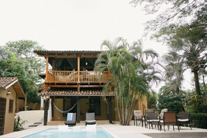 Ein zweigeschossiges Gebäude mit Balkon, Pool und Außenbestuhlung.