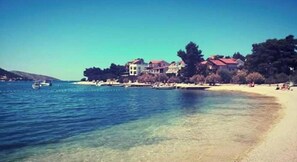 A coastal scene with a clear beach, a few boats, and buildings with red roofs. - One Bedroom Apartment with Sea View and Garden (Šibenik)