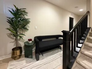 A staircase with a black handrail, a black sofa, a potted plant, and a small table with a red flower.