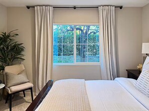 A bedroom with a large bed, a chair, a nightstand, a lamp, and a window with curtains. - Stylish SoCal Getaway - Relax & Unwind (Pomona)