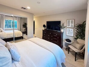 A bedroom with a bed, a dresser, a TV, and a chair.