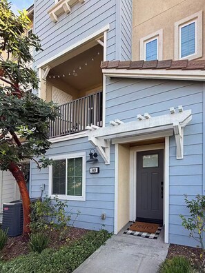 A two-story residential building with a dark front door, a visible mailbox, and a small porch with a railing.
