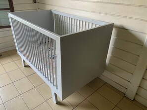A metal crib with vertical bars, positioned against a wall with a tiled floor.