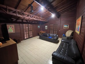 A room with a high ceiling, wooden beams, a black leather sofa, a small round table, and a television.