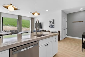 A modern kitchen with a dishwasher, a dining area with a table and chairs, and a view of the outdoors.