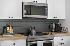 Une cuisine moderne équipée d’une cuisinière en acier inoxydable, d’une bouilloire, d’une machine à café et d’un four à micro-ondes.