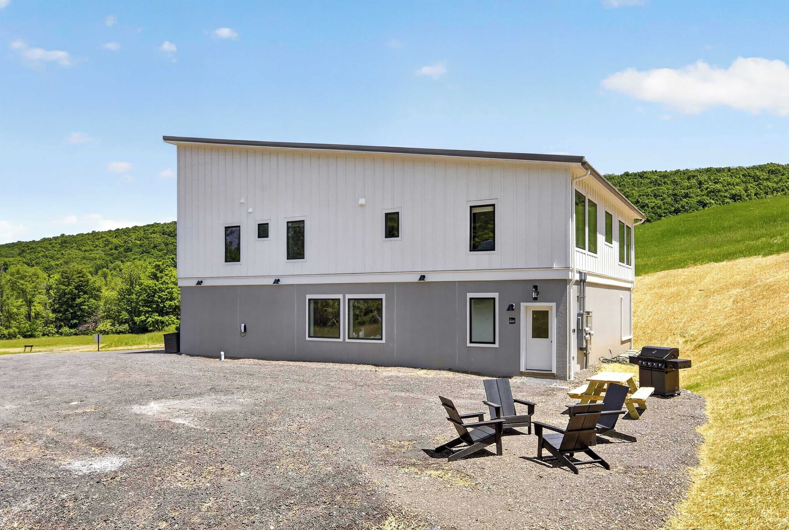Un bâtiment à deux étages avec une allée en gravier et un espace extérieur aménagé pour s’asseoir.