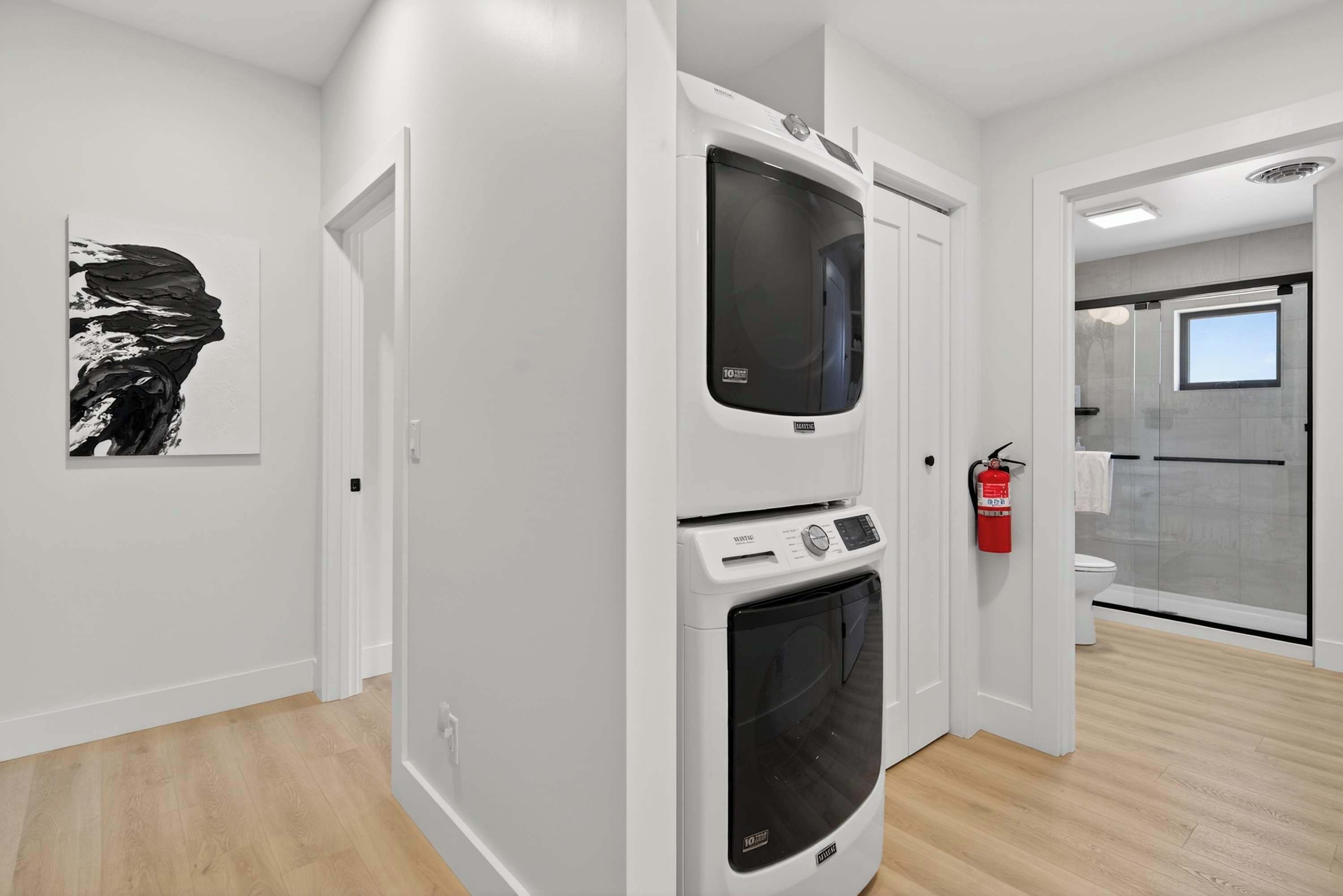 A modern bathroom with a glass shower enclosure, a white toilet, and a wall-mounted fire extinguisher.