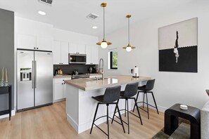 A modern kitchen with white cabinetry, a stainless steel refrigerator, a microwave, and a large island with bar stools.