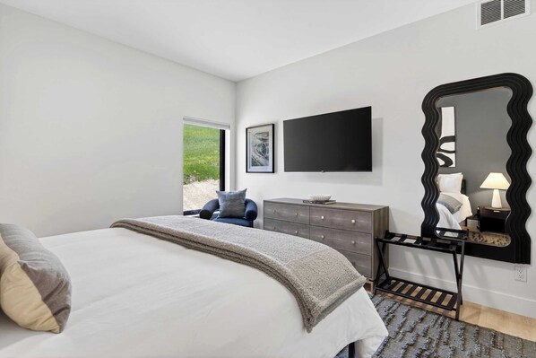 A bedroom with a bed, a dresser, a chair, a large mirror, and a television on the wall.