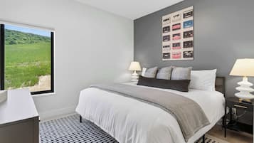 Une chambre avec un grand lit, deux lampes de chevet, une vue sur un paysage verdoyant par la fenêtre et un mur orné d’une œuvre d’art représentant des cassettes audio.