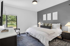A modern bedroom with a bed, bedside tables, a desk, and a large window.