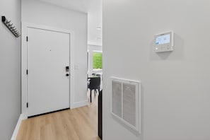 Ein Korridor mit einer weißen Tür, einem an der Wand montierten Thermostat und einem Lüftungsgitter.