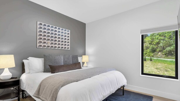 A bedroom with a bed, two bedside tables, a wall-mounted artwork, and a window with a view of greenery. - The Upstate Loft- Close to Ithaca, Cornell, and IC (Newfield)