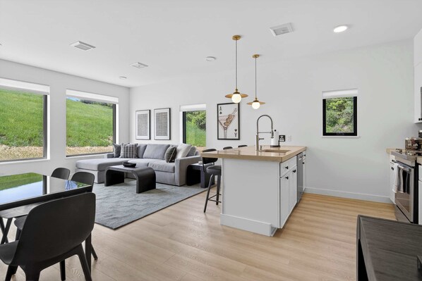 A modern kitchen with a central island, a dining area with a table and chairs, and a living room with a sofa and a coffee table.