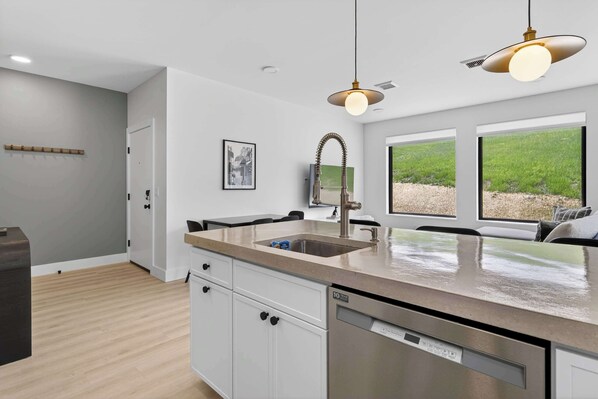 A modern kitchen with a built-in dishwasher, a stainless steel sink, and pendant lighting.