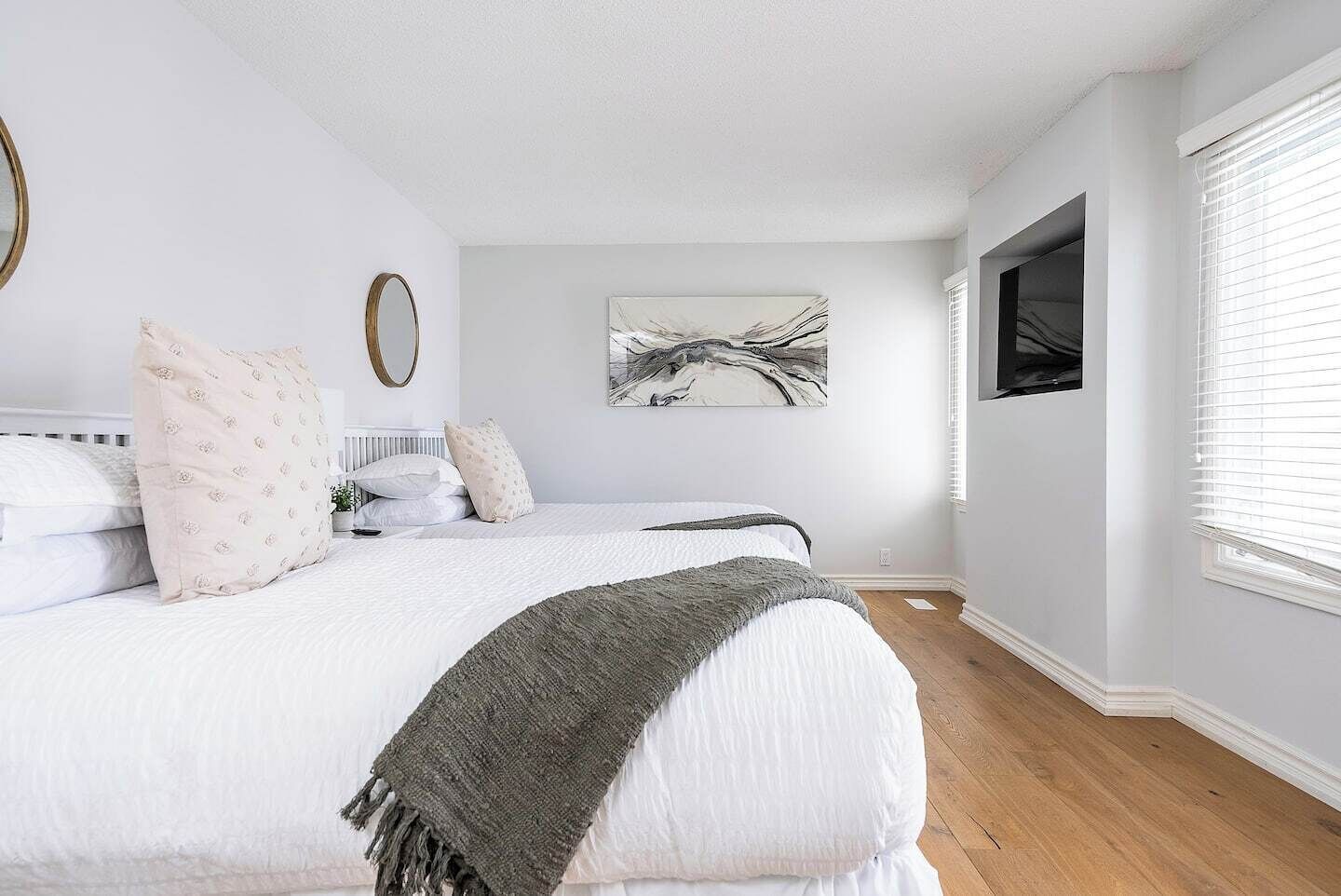 Une chambre à coucher avec un grand lit, une table de chevet, un miroir, une œuvre d’art accrochée au mur et une fenêtre avec des stores.