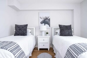 Un dormitorio con dos camas, una mesita de noche, una lámpara y un cuadro de un alce.