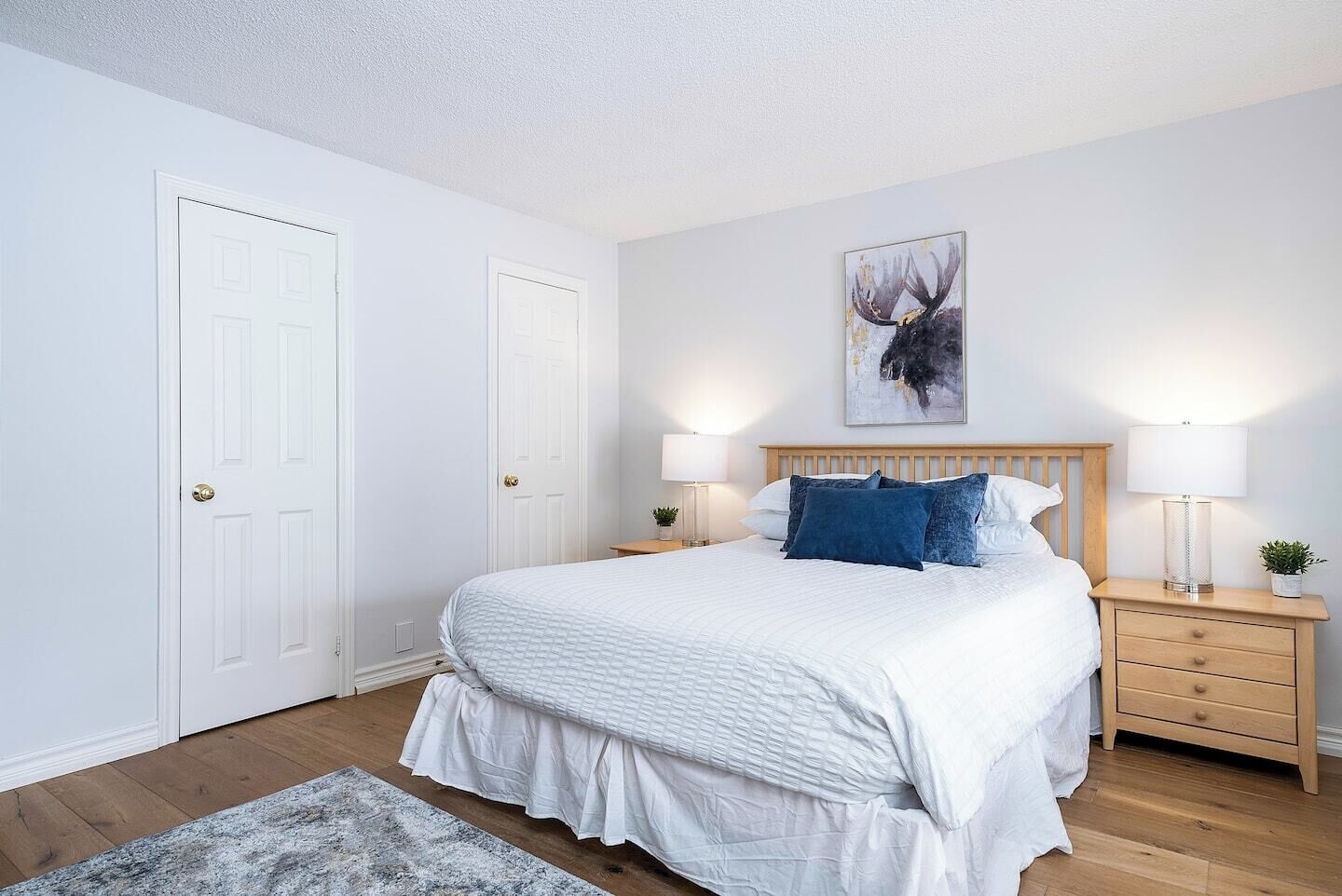 A bedroom with a bed, two bedside tables, a nightstand, a wall-mounted lamp, and a framed picture.
