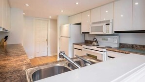 Uma cozinha moderna com armários brancos, uma pia de aço inoxidável e um micro-ondas.