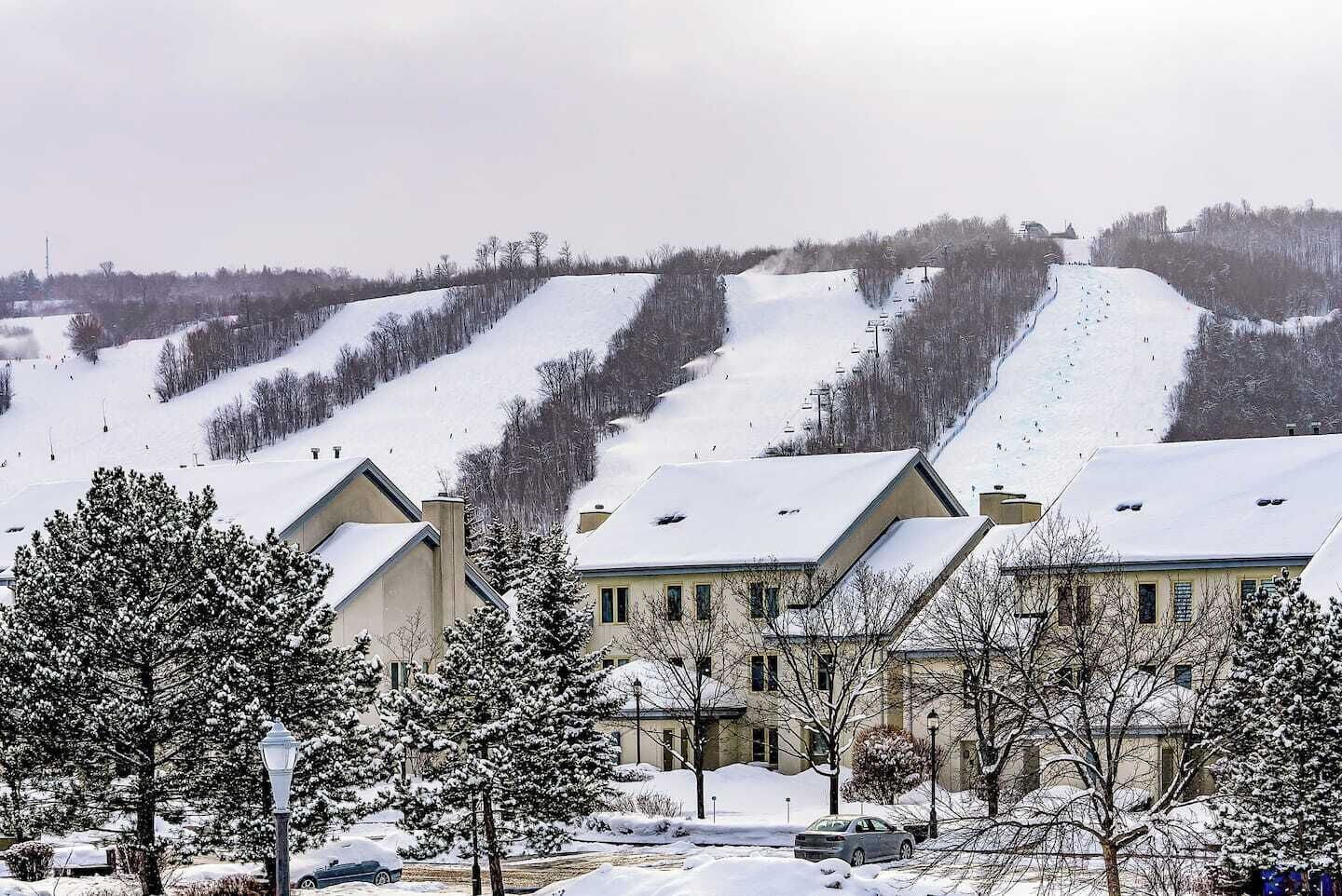 Ein Wohngebiet mit schneebedeckten Häusern und einer Skipiste im Hintergrund.