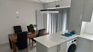 Ett modernt kök med en inbyggd tvättmaskin, en matplats med ett träbord och stolar samt en hänglampa ovanför bordet.