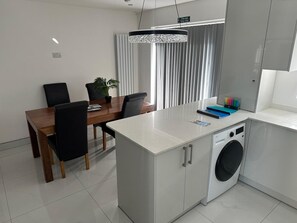 A modern kitchen with a built-in washer, a dining area with a wooden table and chairs, and a pendant light above the table. - House Sleeps 2 With Parking (Slough)