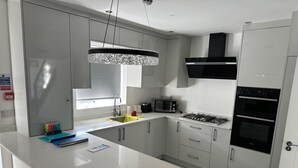 Ett modernt kök med en central köksö, rostfria vitvaror och en hängande lampa.