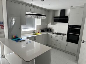 A modern kitchen with a central island, stainless steel appliances, and a pendant light. - House Sleeps 2 With Parking (Slough)