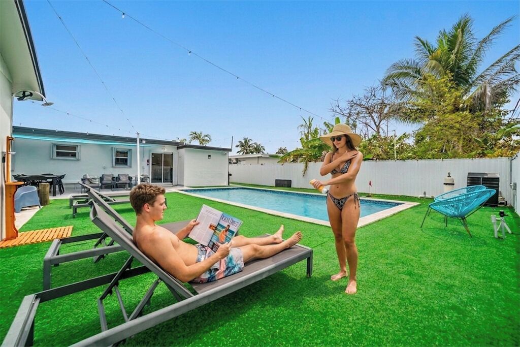 A poolside area with artificial grass, a lounge chair, and a person reading a magazine.