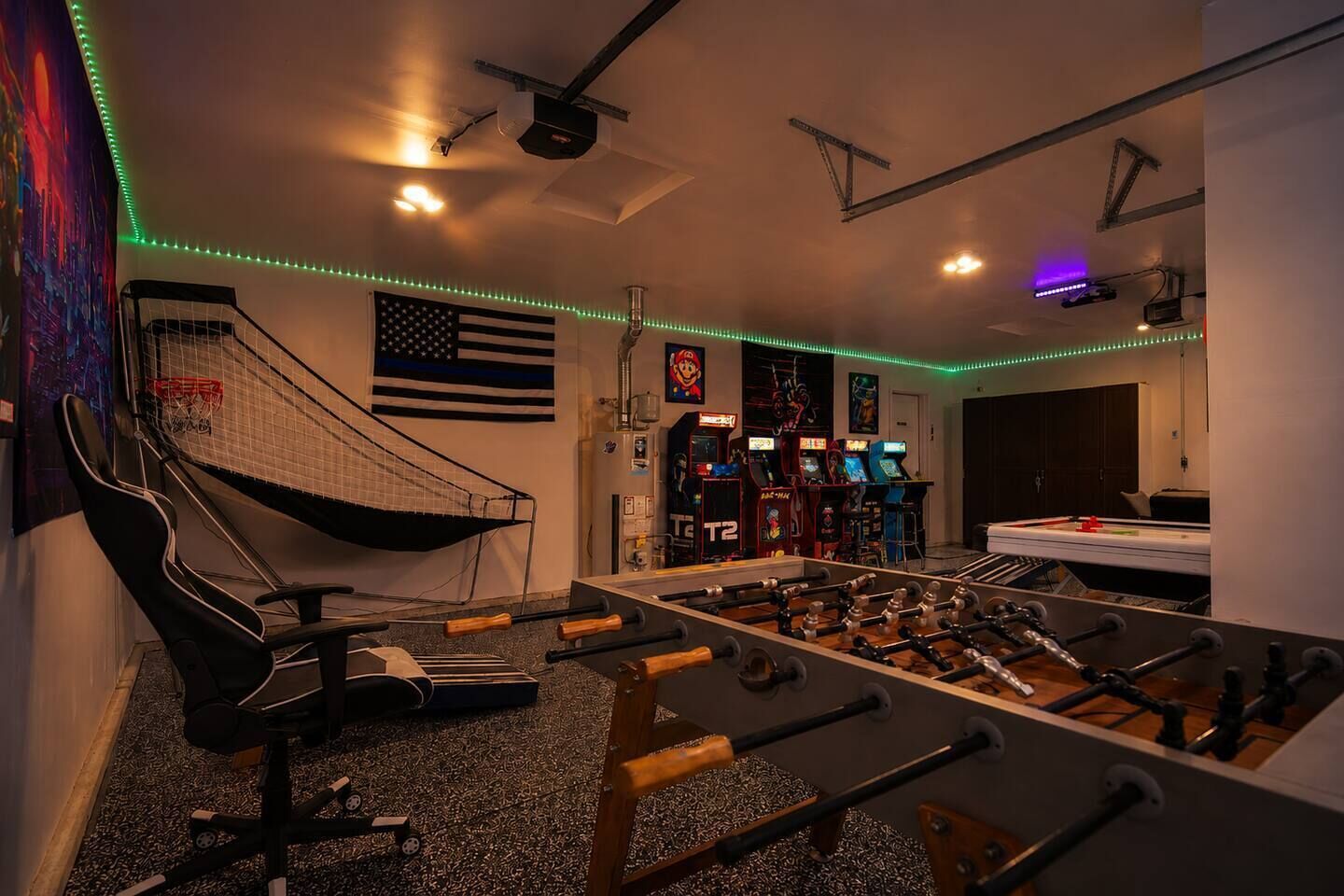 A room with a foosball table, a gaming chair, and arcade machines.
