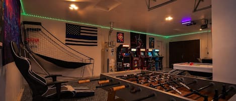 A room with a foosball table, a gaming chair, and arcade machines.