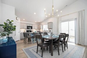 A modern kitchen with a dining area, featuring a chandelier, a potted plant, and a view through the window. - Arcade • Covered Patio • Fire pit • Sleeps 10 (Nampa)