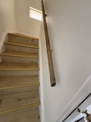 A wooden staircase with a handrail against a white wall.