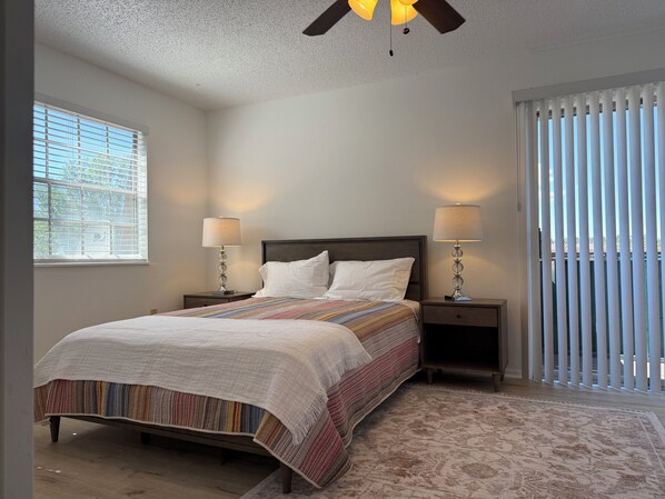 A bedroom with a bed, two bedside tables, a ceiling fan, and a window with blinds.