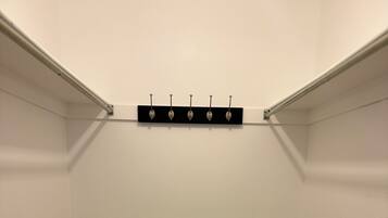 A corner closet with a wooden floor, white walls, and a black shelf with hooks.