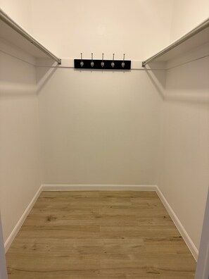 A corner closet with a wooden floor, white walls, and a black shelf with hooks.