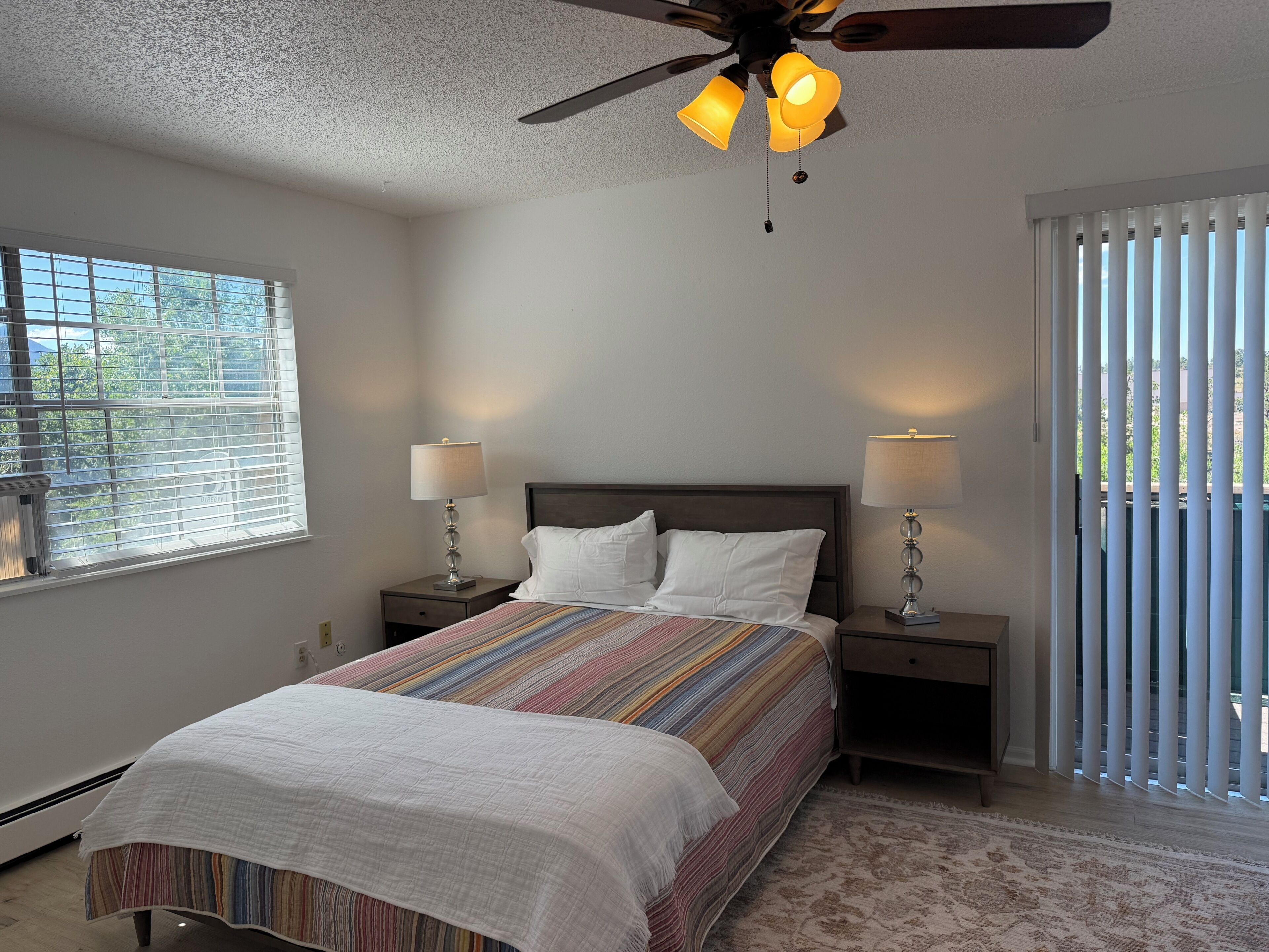 A bedroom with a bed, two bedside tables, a ceiling fan, and a window with blinds.