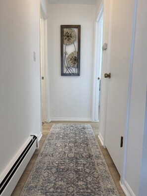 A hallway with a patterned rug, a framed artwork on the wall, and a door at the end.