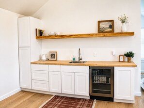 A kitchen with white cabinets, a wooden countertop, a dishwasher, and a wine cooler.