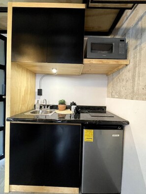 Una cocina compacta con un refrigerador negro, un microondas y un lavamanos.