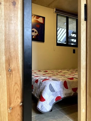 A bedroom with a bed, a window, and a painting on the wall.
