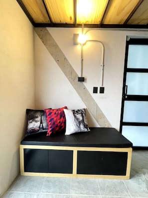A corner room with a black cushioned bench, a wooden ceiling, and a light fixture.
